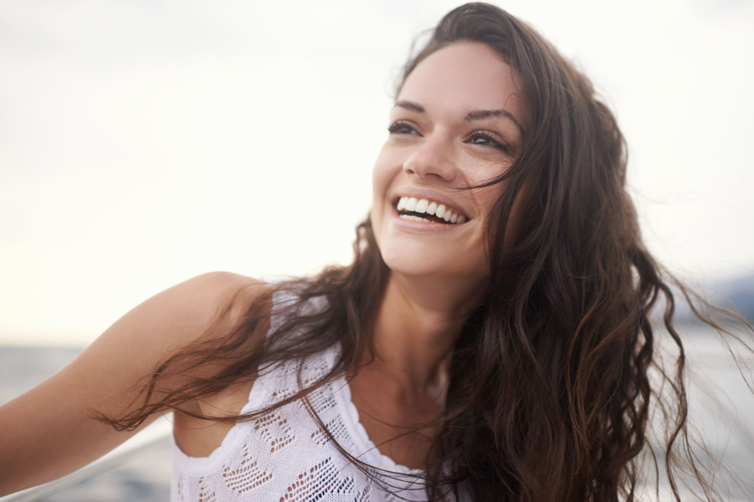 Brunette woman in a white tanktop smiles because she has good oral health and overall health