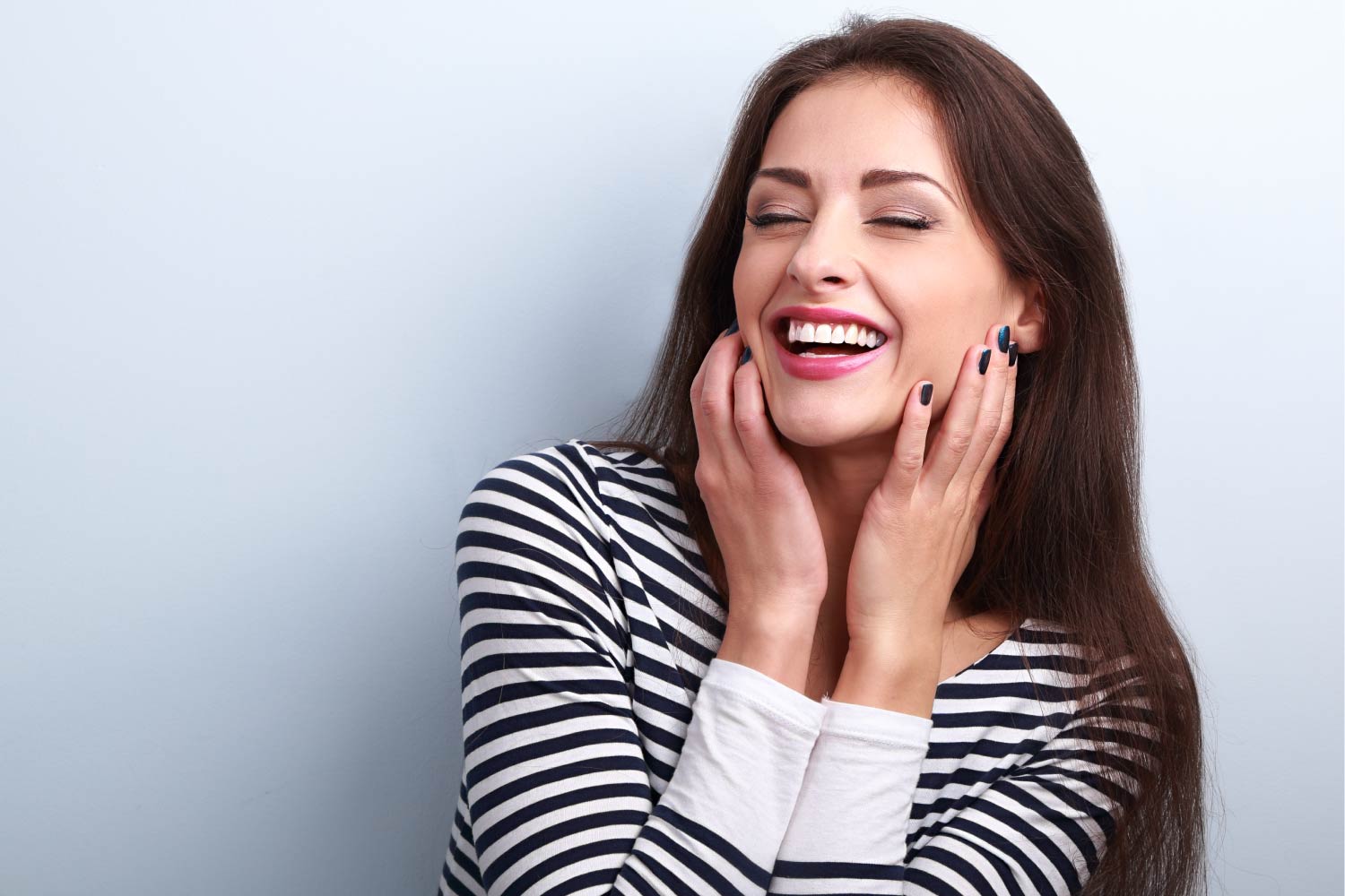 Brunette woman in a striped shirt smiles with her perfect smile after cosmetic dentistry