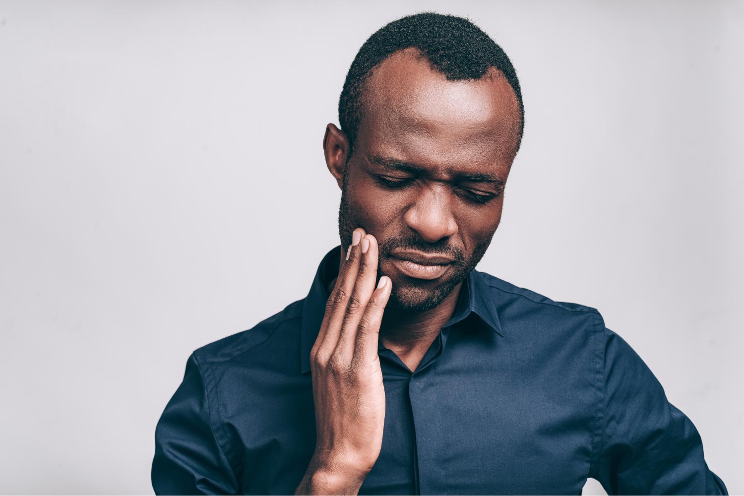 Dark-haired man cringes in pain and touches his cheek due to a toothache in Cedar Park, TX