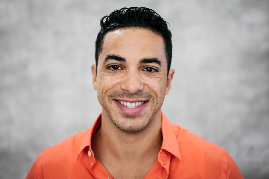 Brunette man in an orange shirt smiles after cosmetic dentistry in Cedar Park, TX