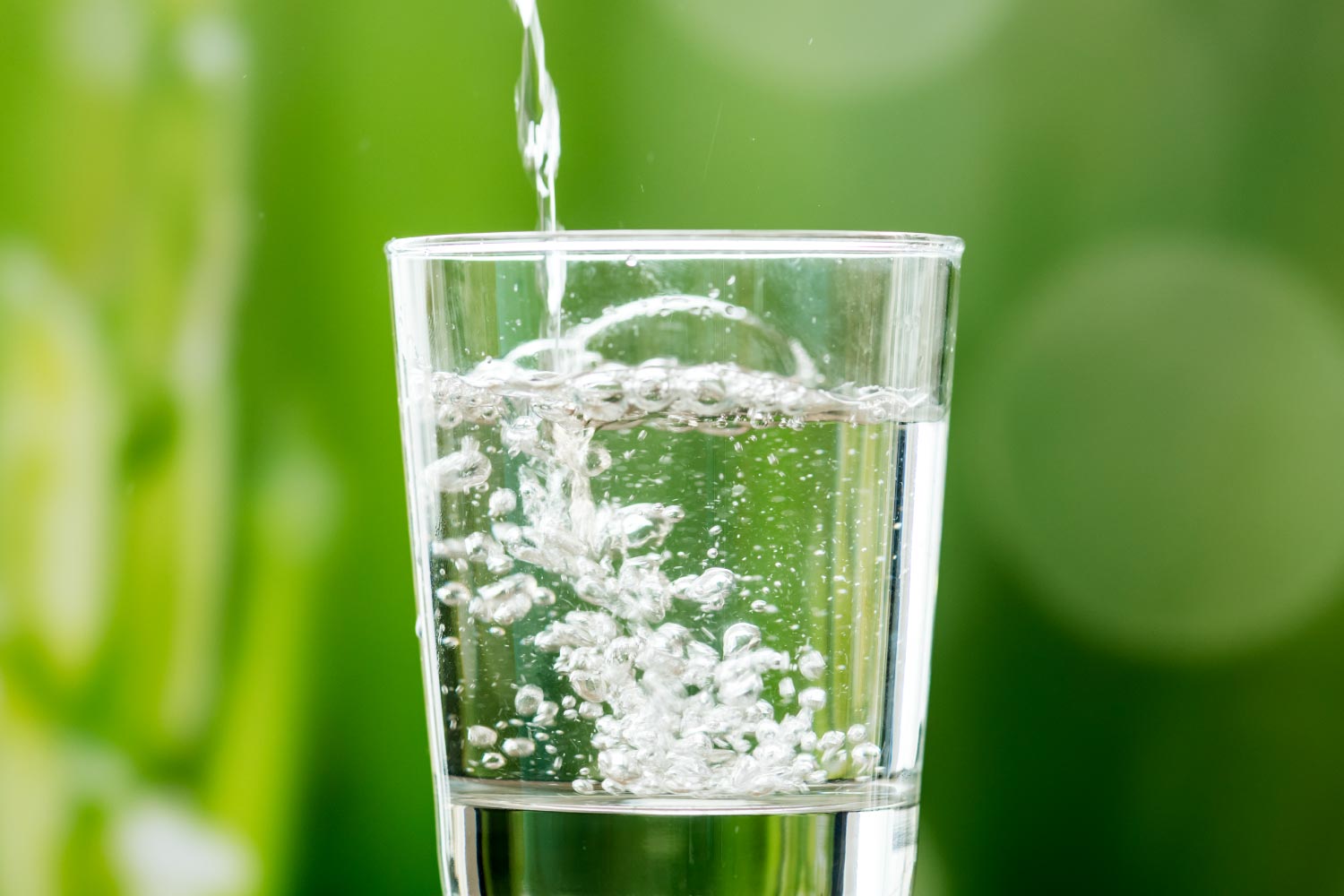 Side view of water being poured into a glass against a green background