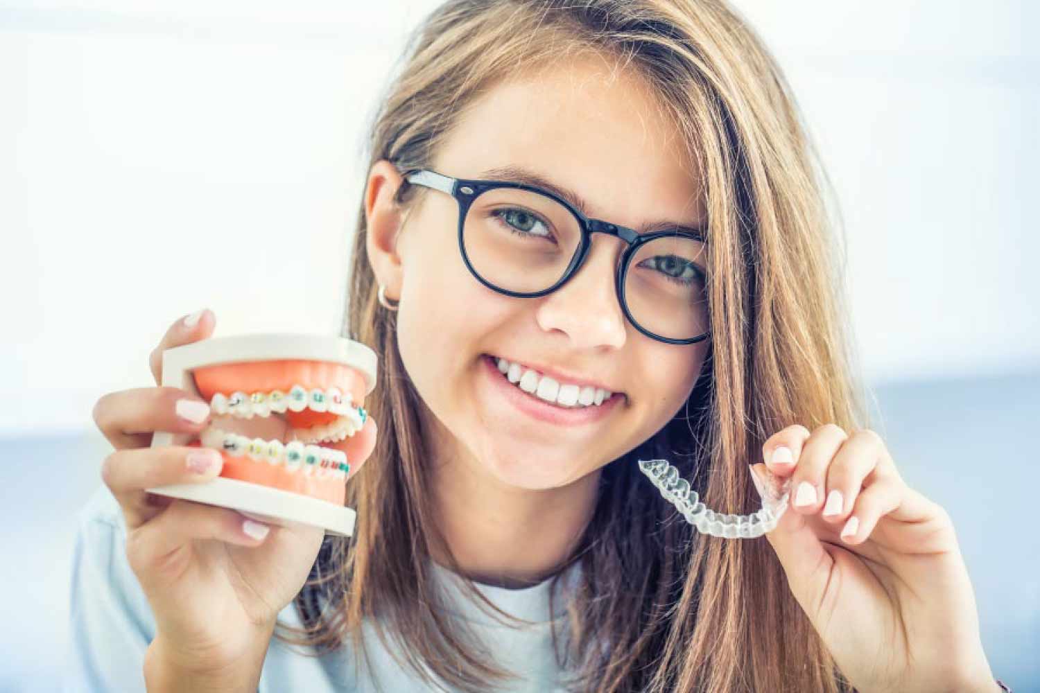 Smiling girl holding model with braces and a clear aligner.
