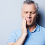 Photo of a man holding his hand to his cheek due to tooth pain.