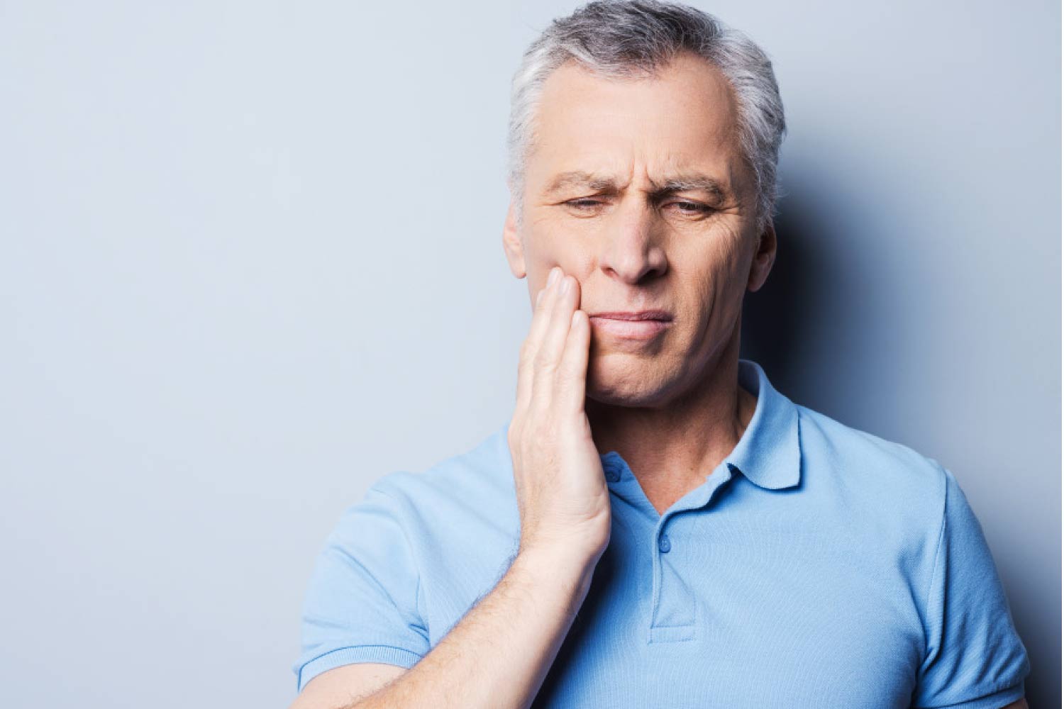 Photo of a man holding his hand to his cheek due to tooth pain.